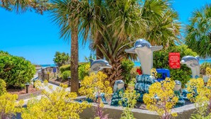 Een tuin met sculpturen van dolfijnen, palmbomen en gele bloemen.