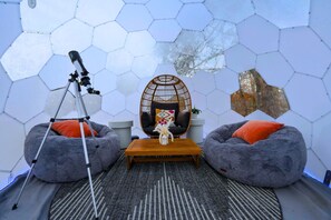 A room with hexagonal ceiling panels, a telescope, two bean bags, a wooden table, and a hanging chair.