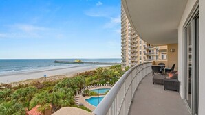 Ein Balkon mit Blick auf Strand und Meer, ein Pool und Gartenmöbel.