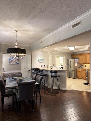 A modern kitchen with a central island, bar stools, and a dining area with a chandelier.