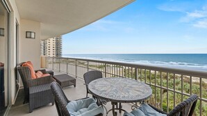 Ein Balkon mit Korbmöbeln und einem Mosaiktable, mit Blick auf einen Strand und den Ozean.