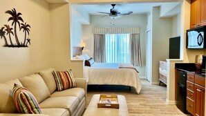 Ein Hotelzimmer mit einer Couch, einem Bett, einem Fernseher und einem Deckenventilator.