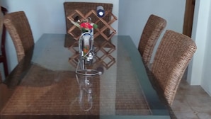 A dining table with wicker chairs, a glass top, and a decorative item on the wall. - Family size of 6 persons,  extra bed upon requestor , Beach front (Anse Boileau)