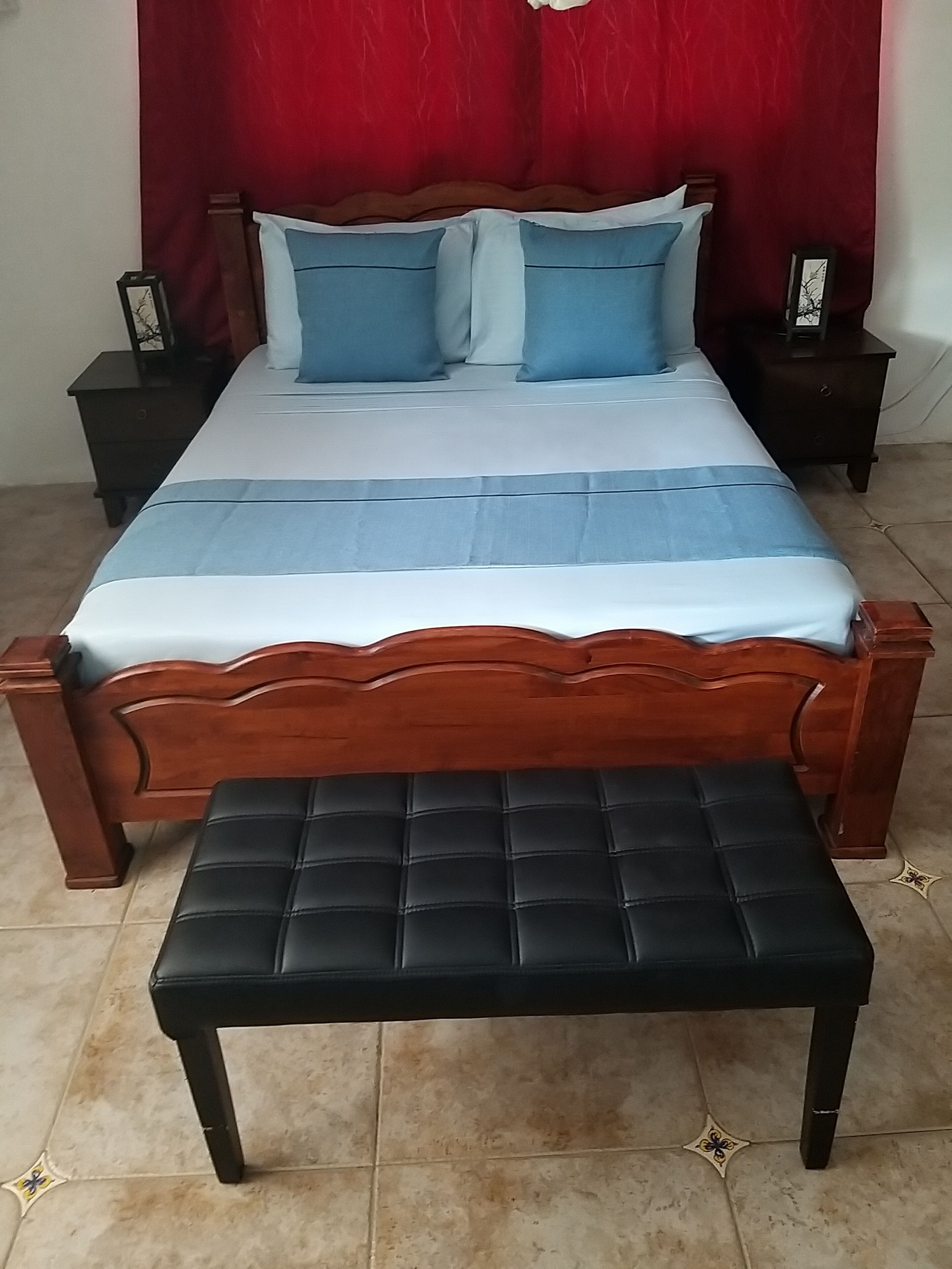 Une chambre à coucher avec un lit en bois, une literie bleue et blanche, deux tables de chevet et un banc noir.