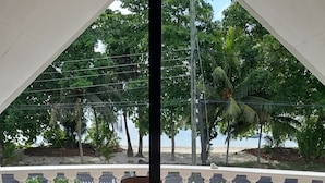 A covered outdoor seating area with a table and chairs, a white railing, and a view of a beach and palm trees. - Family size of 6 persons,  extra bed upon requestor , Beach front (Anse Boileau)