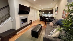 Una sala de estar moderna con chimenea, televisor de pantalla plana y comedor, con una cocina al fondo.