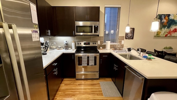 Una cocina moderna con electrodomésticos de acero inoxidable, muebles oscuros y piso de madera.