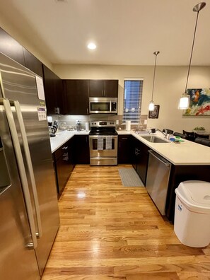 A modern kitchen with stainless steel appliances, dark cabinetry, and a wooden floor.