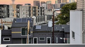 Una terraza en la azotea con una planta en maceta, paneles solares y vistas del horizonte de la ciudad al atardecer.