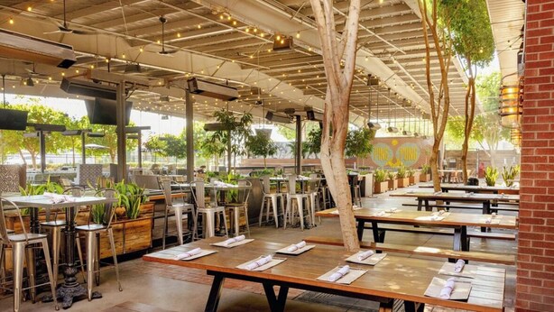 An outdoor restaurant with wooden tables and benches, potted plants, and a brick wall. - Walkable Historic Phoenix Casita + Private Pool (Phoenix)