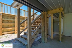 A wooden staircase leading to a covered outdoor area with a metal roof, surrounded by wooden fences.