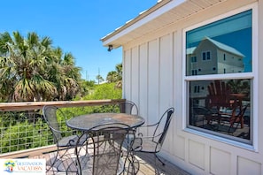 A balcony with a table and chairs, a view of a house, and a palm tree.