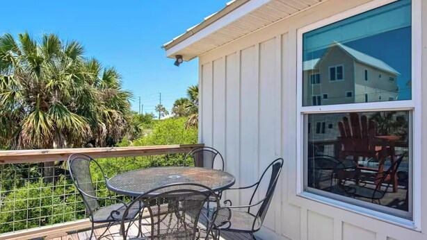 A balcony with a round metal table and chairs, a view of a house through a large window, and a palm tree in the background. - Spacious 3BR Beach Retreat Sleeps 10 | Family Ready (Port St. Joe)