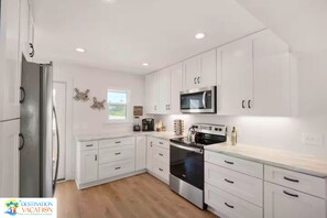 A modern kitchen with white cabinets, a stainless steel refrigerator, a microwave, and an oven. - Ocean View Getaway Steps to Gulf | Family-Friendly 3BR (Port St. Joe)