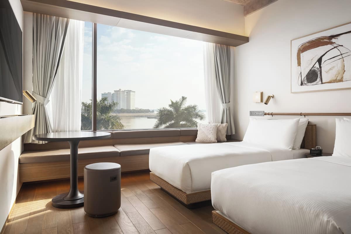 Ein Hotelzimmer mit großem Fenster, zwei Betten, einem kleinen Tisch und einem Mülleimer.