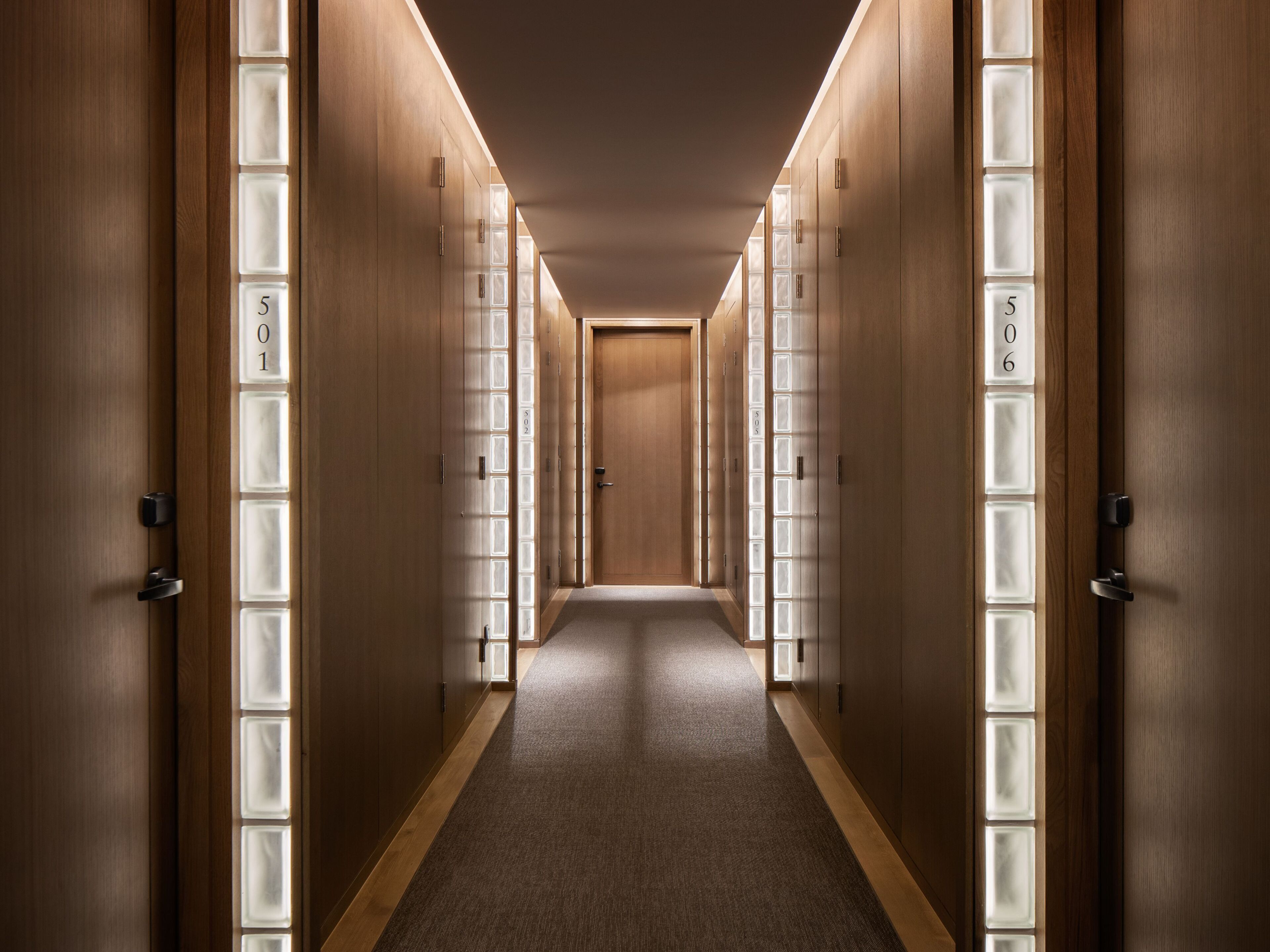 A hotel corridor with wooden doors and frosted glass panels, each marked with room numbers.