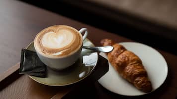 A cup of coffee with latte art on a saucer, a croissant on a plate, and a spoon.