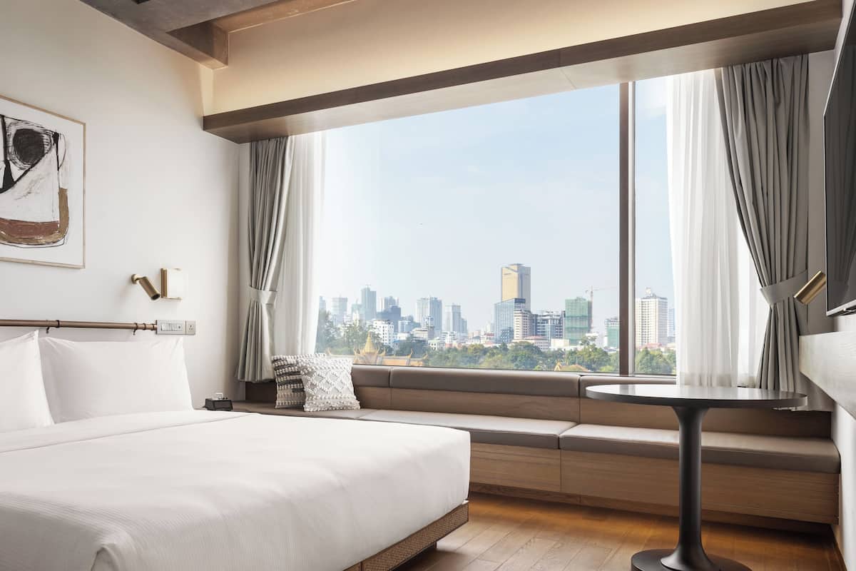 Ein Hotelzimmer mit einem großen Bett, einer Sitzecke mit Blick auf die Stadt und einem kleinen Tisch.