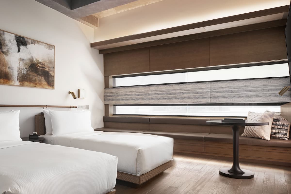 Ein modernes Hotelzimmer mit zwei Betten, einem kleinen runden Tisch und einem großen Fenster mit Stadtblick.