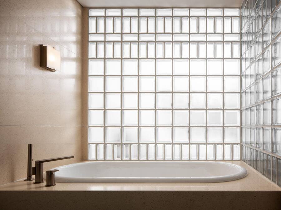 A modern bathroom with a freestanding bathtub, a wall-mounted light, and a glass block partition.