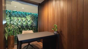 A conference room with a wooden table, a potted plant, and a view of a green wall with foliage.