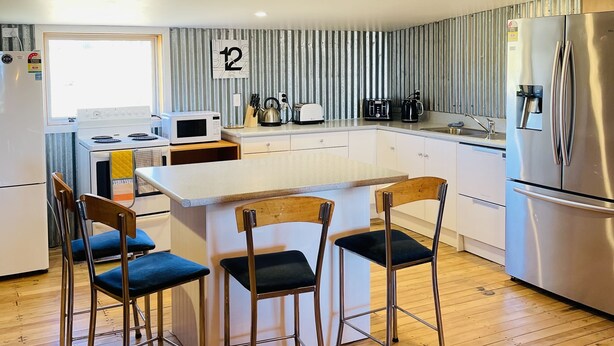 Une cuisine moderne dotée d’un îlot central, de chaises en bois et d’appareils électroménagers en acier inoxydable.