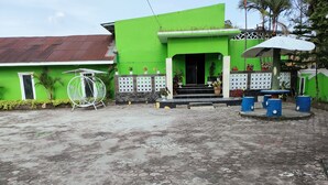 A green building with a tiled entrance, a white chair, and a small outdoor seating area with blue stools. - Hotel Bukit Sentabi Penembahen (Medan)