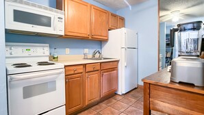 A kitchen with wooden cabinets, a white stove, a microwave, a refrigerator, and a blender on the counter.