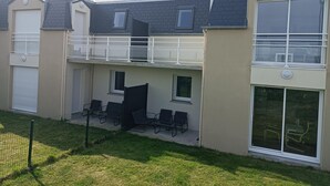 A two-story residential building with a balcony, large windows, and a fenced outdoor area with chairs.