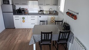 A compact kitchen with grey cabinets, a microwave, a coffee maker, and a sink. There is a dining table with chairs and a radiator on the wall.