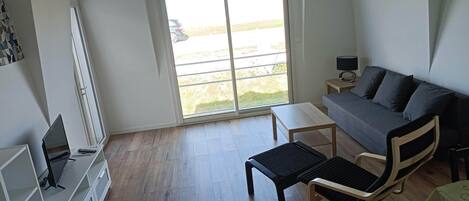 A modern living room with a sofa, a coffee table, a TV, and a sliding glass door to a balcony.