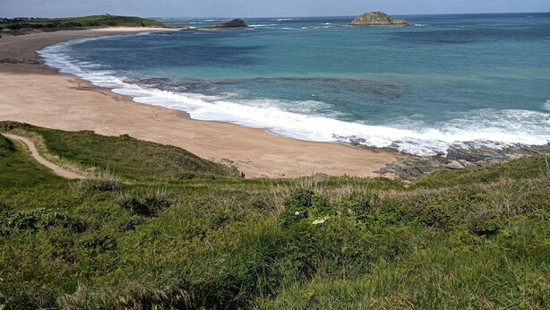 A coastal landscape with a sandy beach, grassy areas, and rocky outcrops.