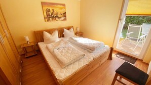 Ein Schlafzimmer mit einem hölzernen Bett, zwei Nachttischen, einem Gemälde an der Wand und Blick ins Freie durch eine Schiebetür.