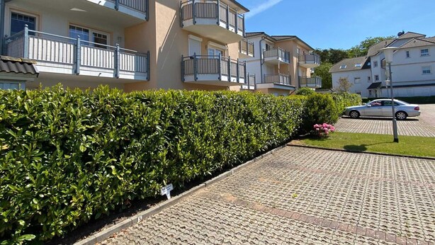 Ein Wohngebäude mit mehreren Balkonen, einer gepflasterten Auffahrt und einer Hecke.