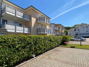 A residential building with multiple balconies, a paved driveway, and a hedge.