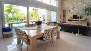Un salon moderne comprenant un coin repas, de grandes fenêtres, un mur en pierre et un canapé noir.