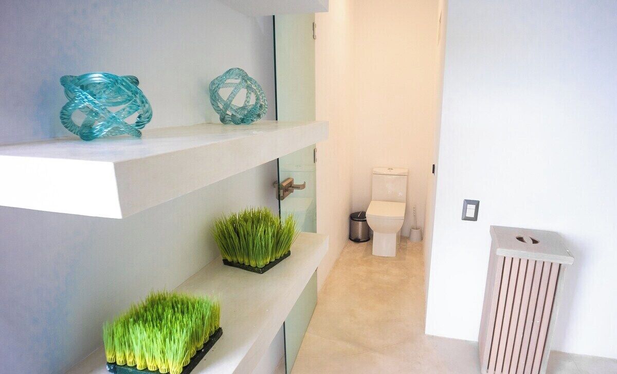 A modern bathroom with a toilet, a trash bin, and decorative items on shelves.