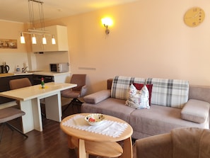 A modern living room with a dining area, a sofa with patterned cushions, a small round table with a bowl, and a wall clock.