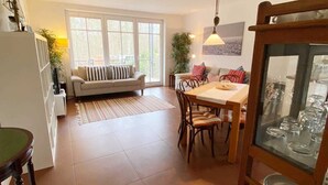 A spacious living area with a sofa, dining table, and chairs. There is a kitchen area with a refrigerator and cabinets. - Vacation apartment Bucheneck 15 (Graal-Müritz)