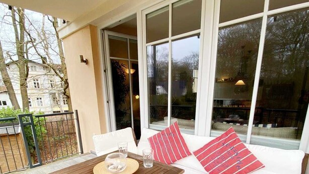 A wooden deck with a table and white sofa with red cushions. - Vacation apartment Bucheneck 15 (Graal-Müritz)