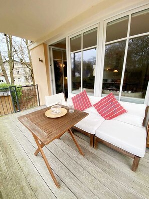 Une terrasse en bois avec une table et un canapé blanc agrémenté de coussins rouges.