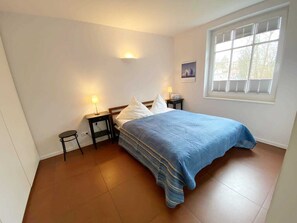 Une chambre à coucher comprenant un lit, deux tables de chevet, une fenêtre et un luminaire fixé au mur.