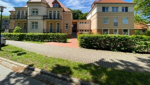A hotel with a central entrance, multiple balconies, and a paved driveway. - Vacation apartment Bucheneck 15 (Graal-Müritz)