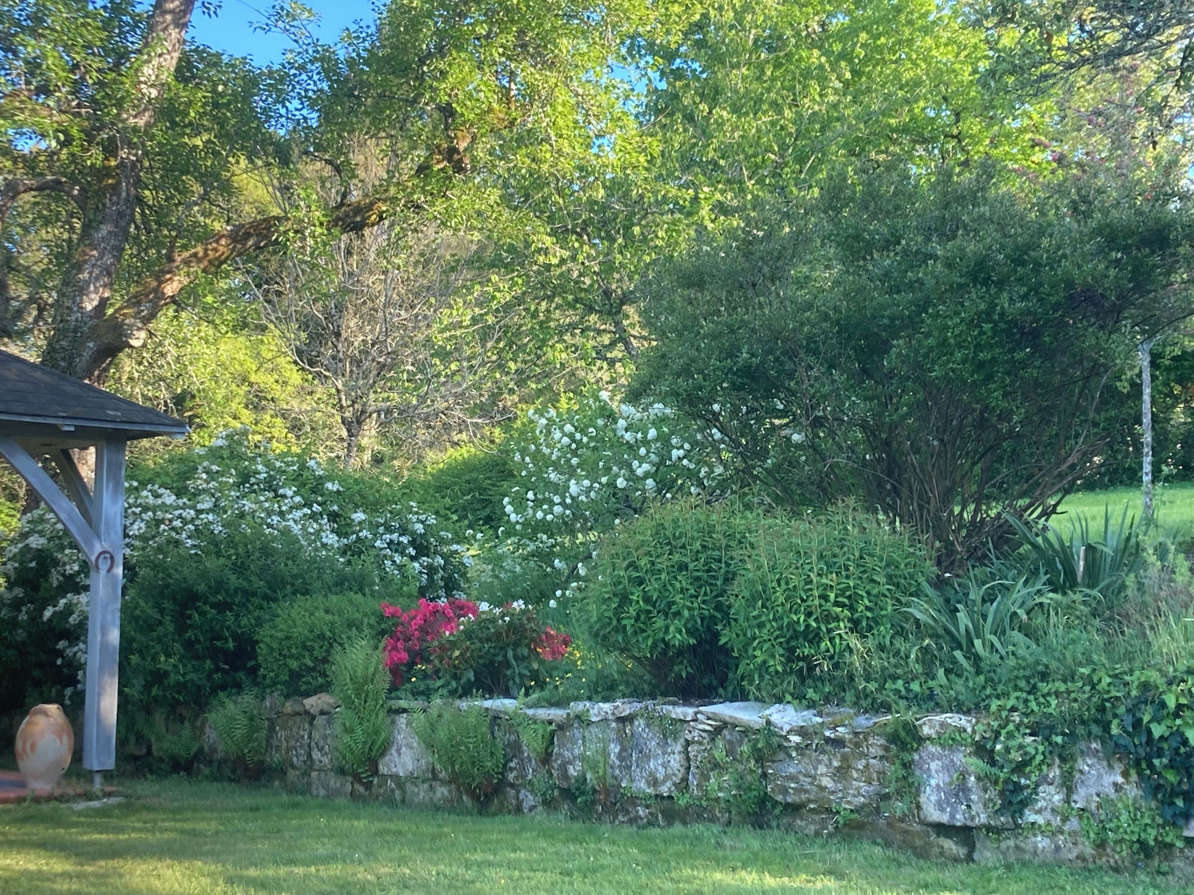 Um jardim com muro de pedra, diversas plantas e um gazebo.