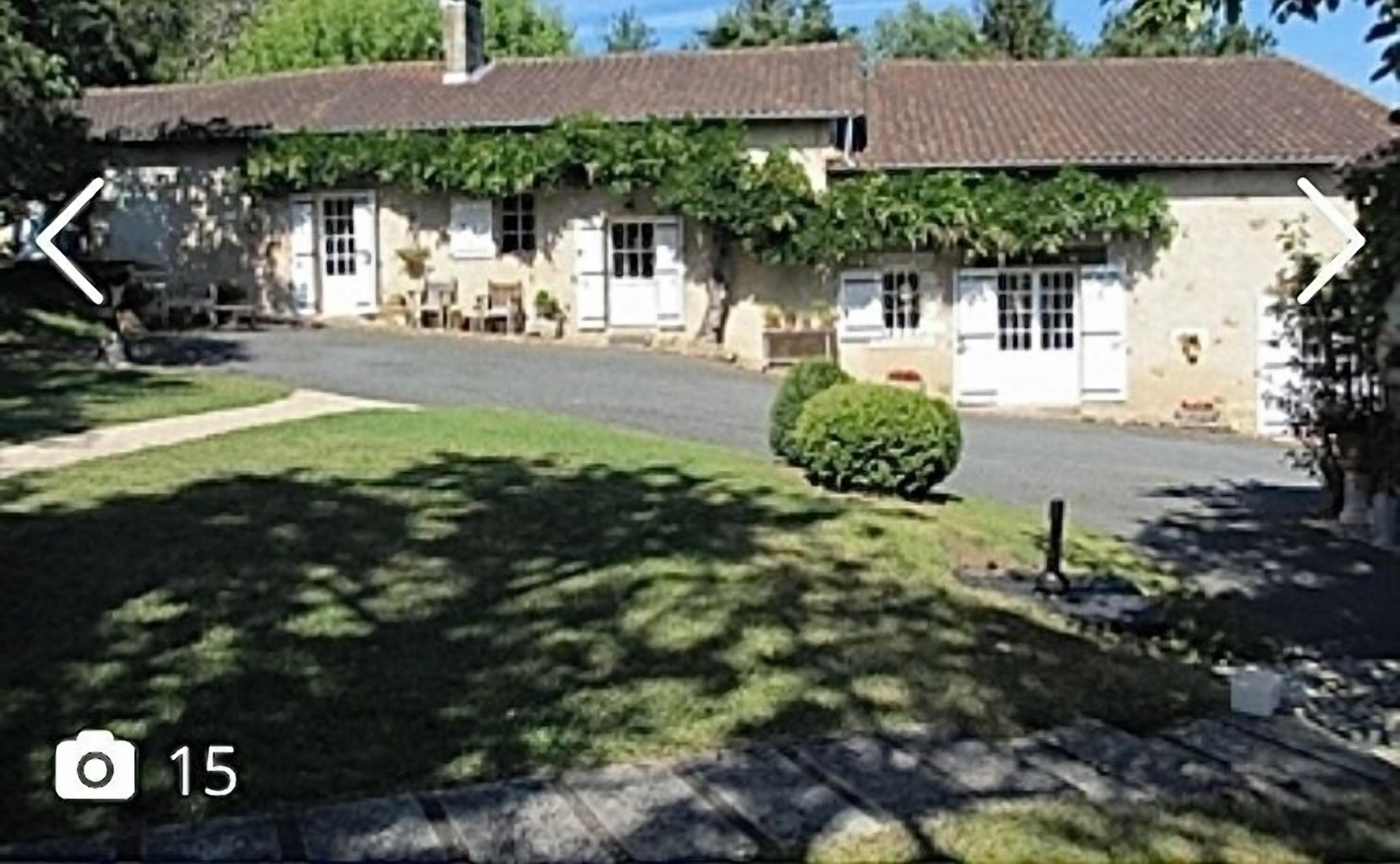 Um edifício de dois andares com telhado de telhas, paredes externas brancas e um pequeno jardim frontal.
