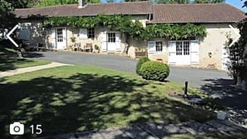 Um edifício de dois andares com telhado de telhas, paredes externas brancas e um pequeno jardim frontal.