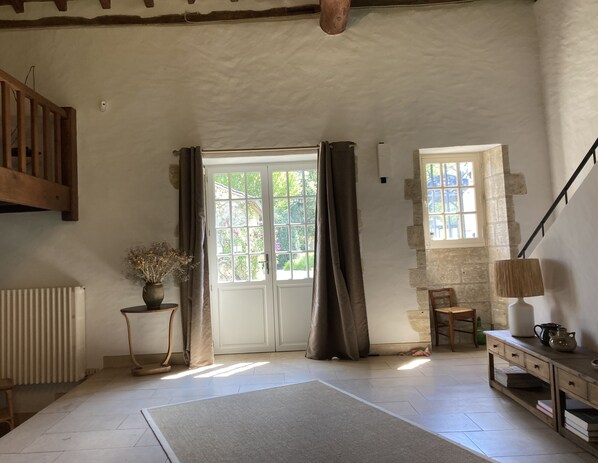 A spacious room with a large window, a wooden staircase, a radiator, and a small table with a lamp.