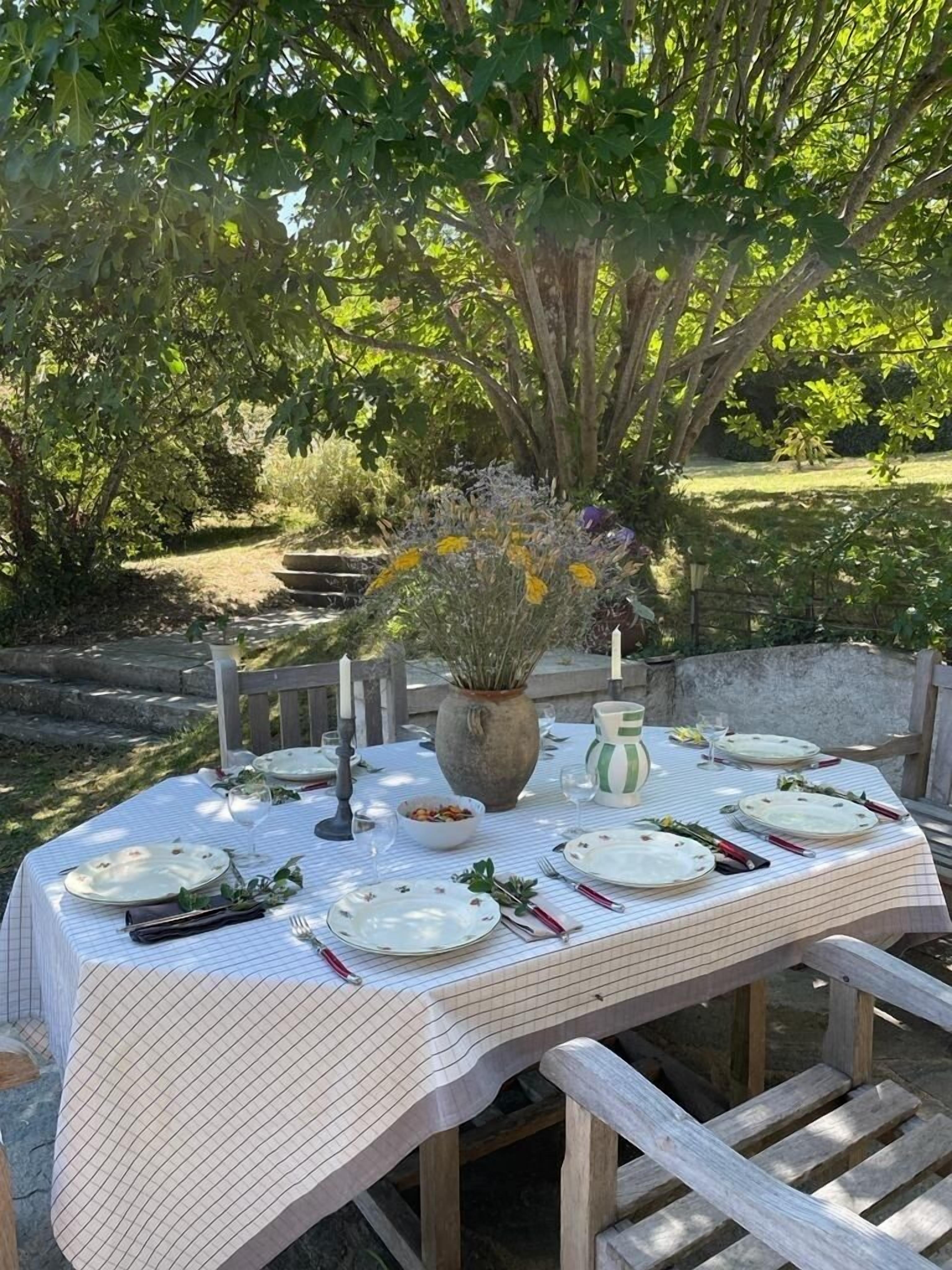 An outdoor dining table set for a meal, surrounded by greenery and trees.