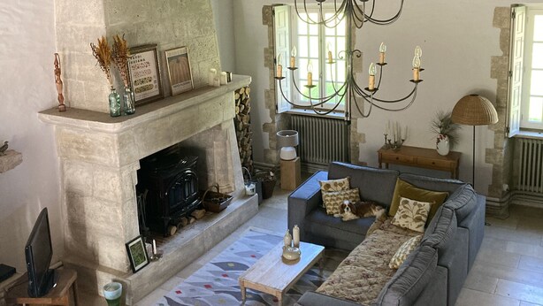 Een landelijke woonkamer met een stenen openhaard, een kroonluchter en een zithoek.
