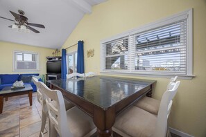 A dining area with a dark wooden table, white chairs, and a ceiling fan.